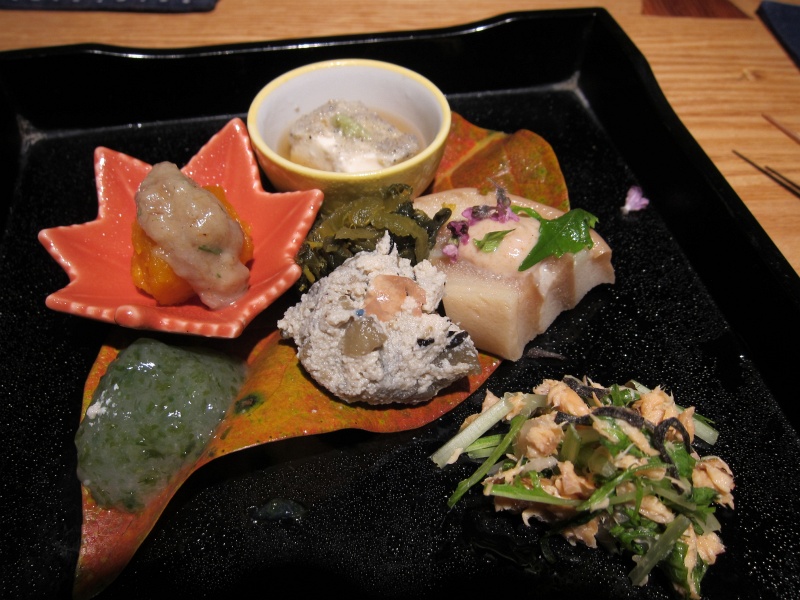 IMG_0194.JPG - The "hassun" course, feature a sample of small dishes on a real red leaf.  Clockwise starting from the red leaf plate: pumpkin with herring fish sauce, tofu with fish powder and wasabi, rice cake/fish cake/gluten with shiso flowers, salmon vegetable scramble, seaweed/scallop konnyaku (gelatin).  In center: seaweed/bacon, tofu scramble with sweet vegetables (dried cherry sliver on top).
